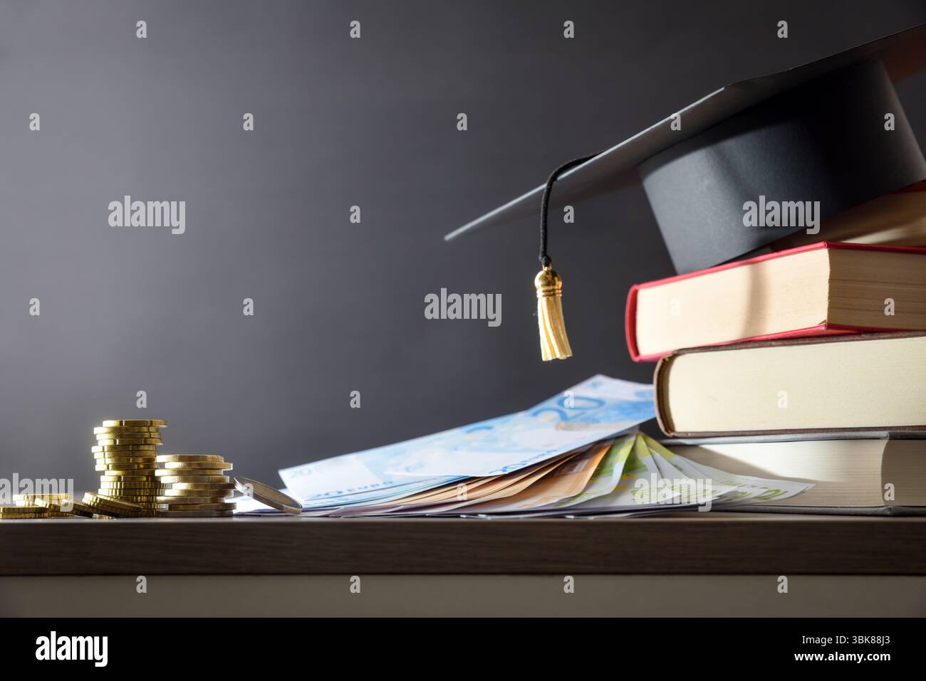 Dettaglio del concetto di spesa per l'istruzione con bacheca su una pila di libri e denaro su un tavolo di legno e sfondo scuro isolato. Vista frontale. Foto Stock