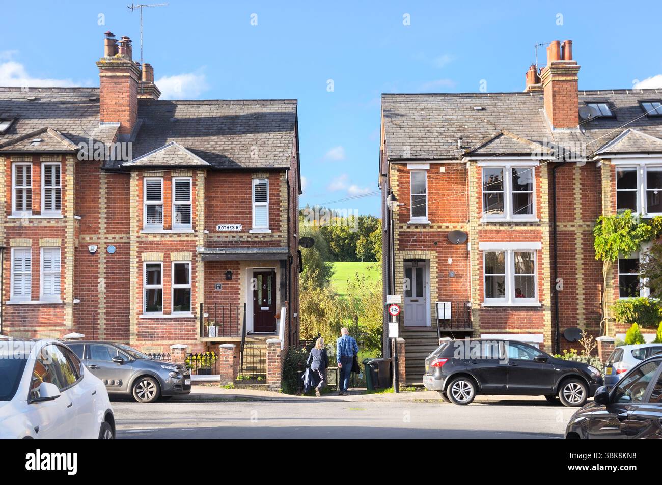 Una coppia che cammina lungo un sentiero/vicolo tra file di case vittoriane a schiera su una strada con campi verdi sullo sfondo, Dorking, Surrey, Inghilterra Regno Unito Foto Stock