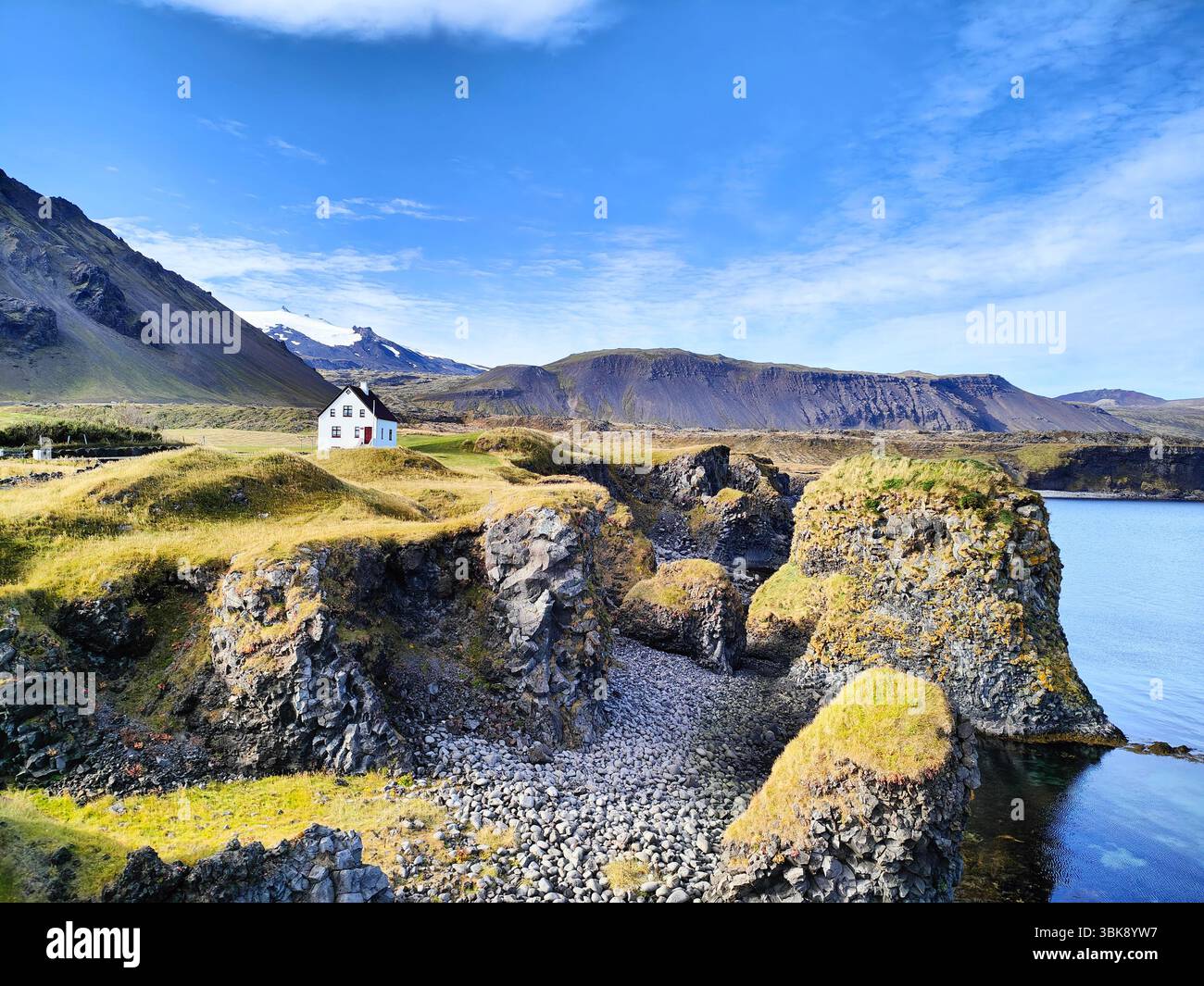 Casa bianca sulle scogliere di Arnarstapi, Islanda, con il vulcano glaciale Snæfellsjökull sullo sfondo e le spettacolari formazioni rocciose costiere. - Immagine stock catturata con smartphone