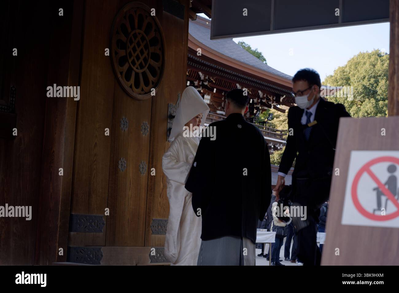 La sposa e lo sposo si fermano in una tranquilla conversazione sotto le orde ornate del santuario Meiji Jingu, mentre il fotografo si muove rapidamente Foto Stock