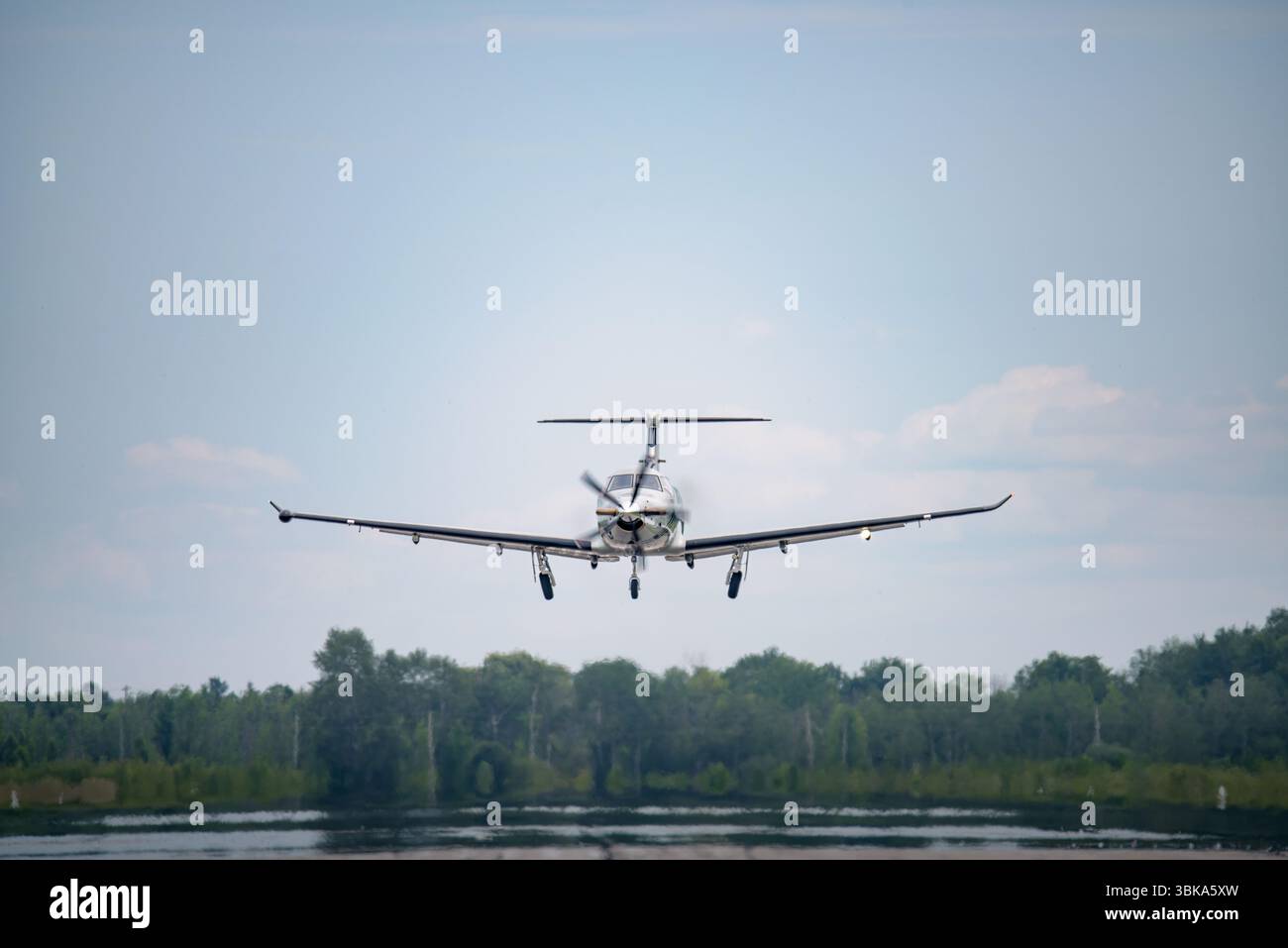 Gli aerei turboelica si stanno appena sollevando dalla pista, i carrelli di atterraggio si estendono mentre si arrampica su un lago calmo e un battistrada lontano. Foto Stock