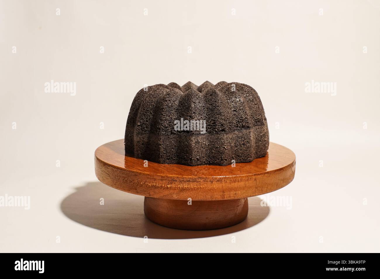 Una torta di riso glutinoso completamente nera posta su un supporto rotondo di legno su uno sfondo neutro. Tradizionale concetto di dessert asiatico. Foto Stock