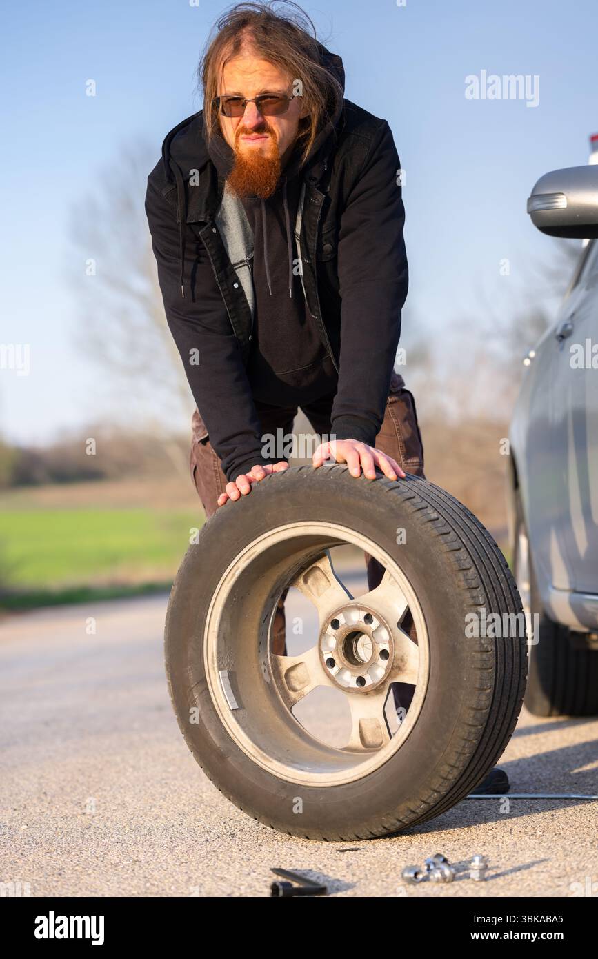 Uomo che tiene la ruota di scorta in prossimità del punto di arresto della strada Foto Stock