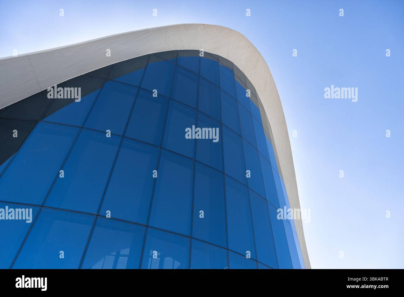 Moderno edificio curvo in vetro contro un profondo angolo blu del cielo Foto Stock