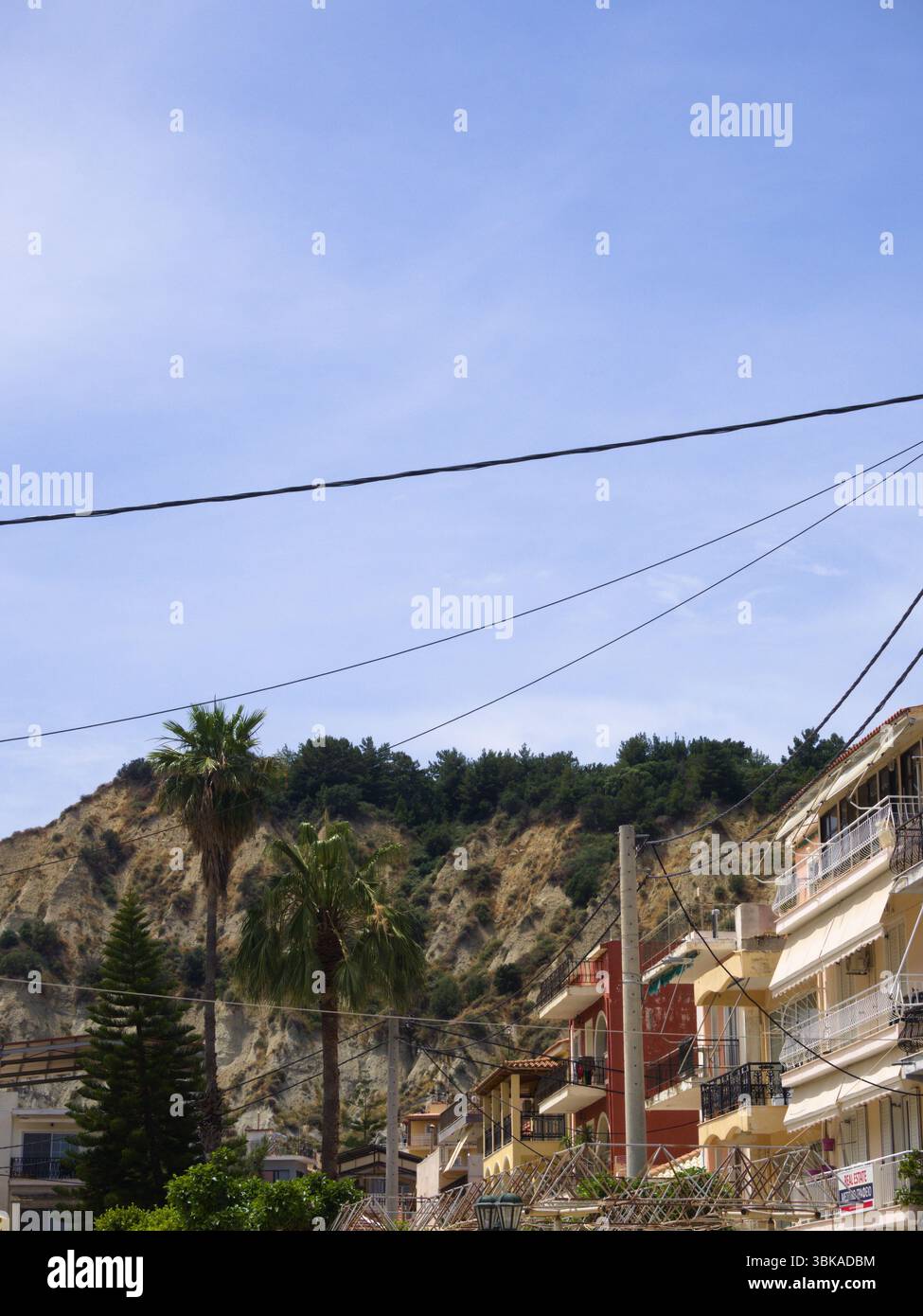 Case colorate e palme nella città di Zante, isola di Zante, Grecia, con una collina rocciosa e un cielo azzurro cristallino sullo sfondo. Foto Stock