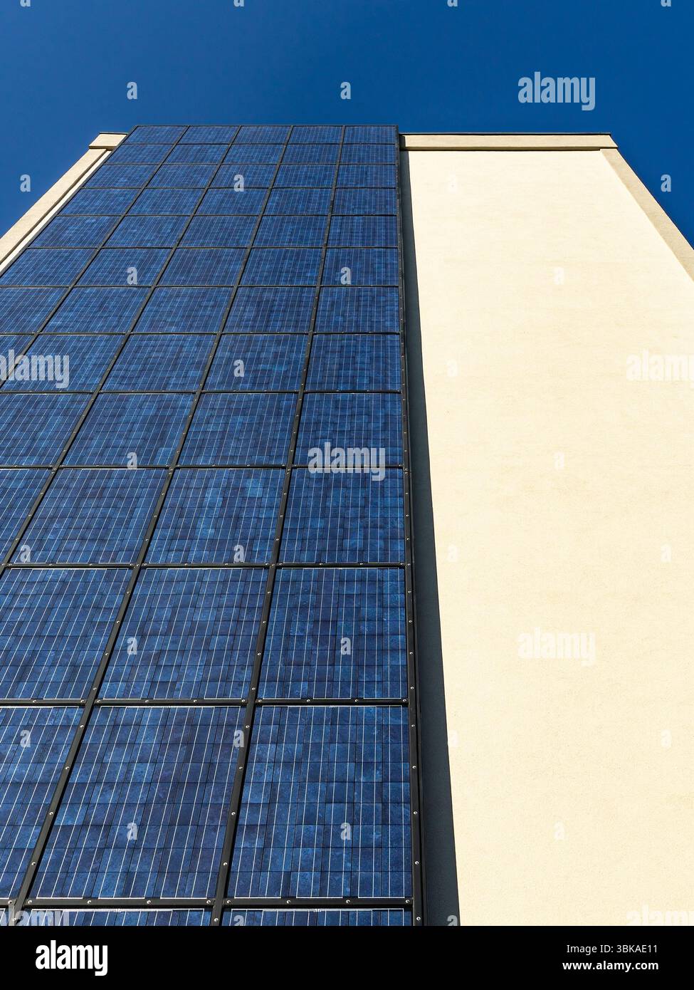 Vista dal basso dei pannelli solari verticali sulla facciata di un moderno edificio urbano sotto il cielo blu, che illustra l'energia pulita e lo sviluppo sostenibile della città. Foto Stock
