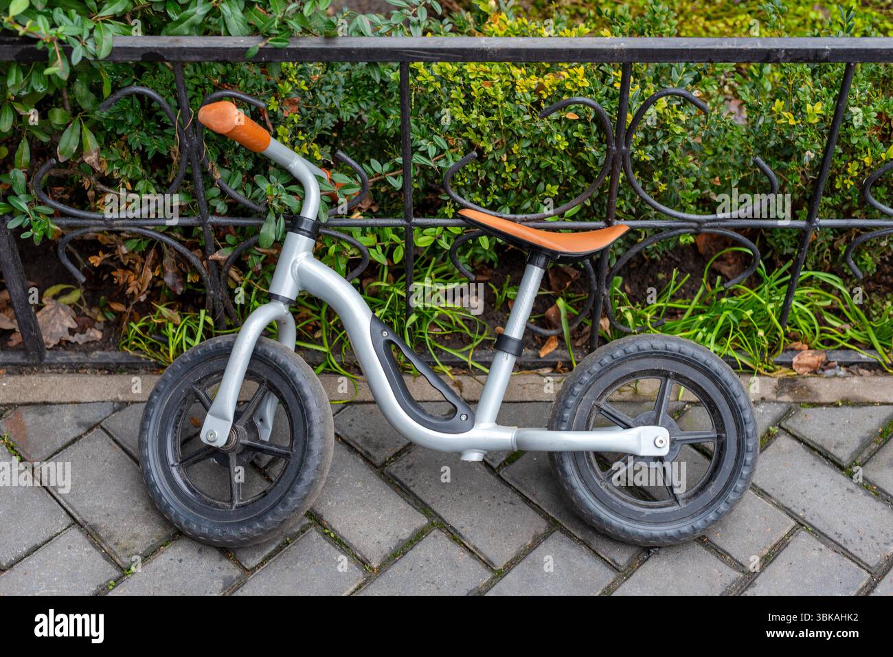 Una bicicletta compatta in metallo per bambini parcheggiata contro una recinzione in ferro battuto in un'area ben curata con pavimentazione e vegetazione Foto Stock