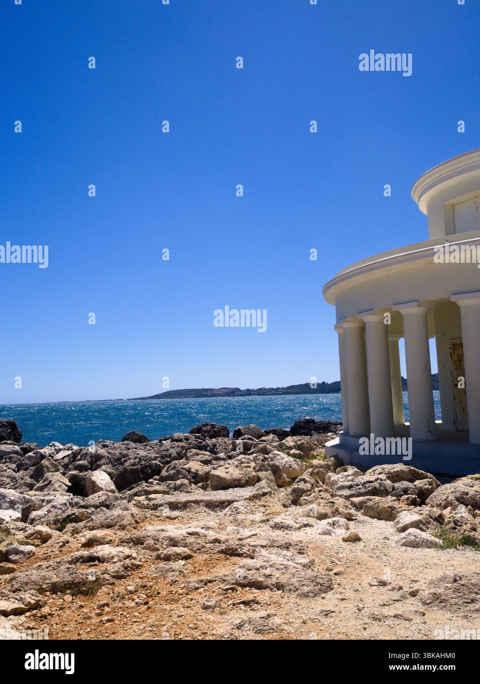Facciata del faro di Saint Theodor, isola di Cefalonia, incorniciata da rocce e mare sotto un cielo senza nuvole. Foto Stock