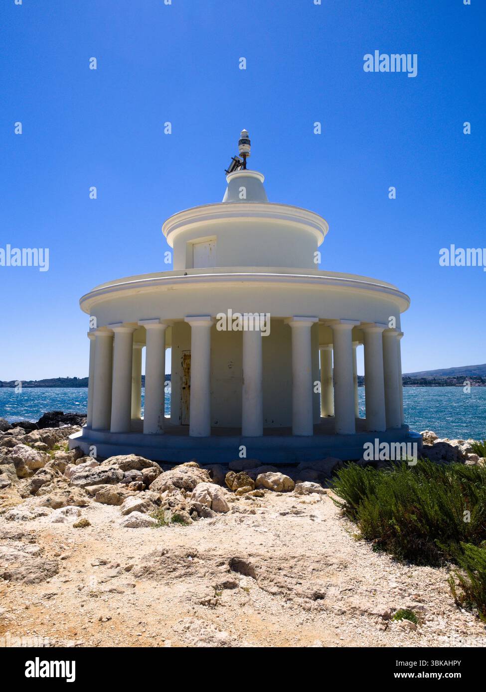 Vista ravvicinata del faro di Saint Theodor a Cefalonia, Grecia, con terreno roccioso, mare e cielo azzurro. Foto Stock