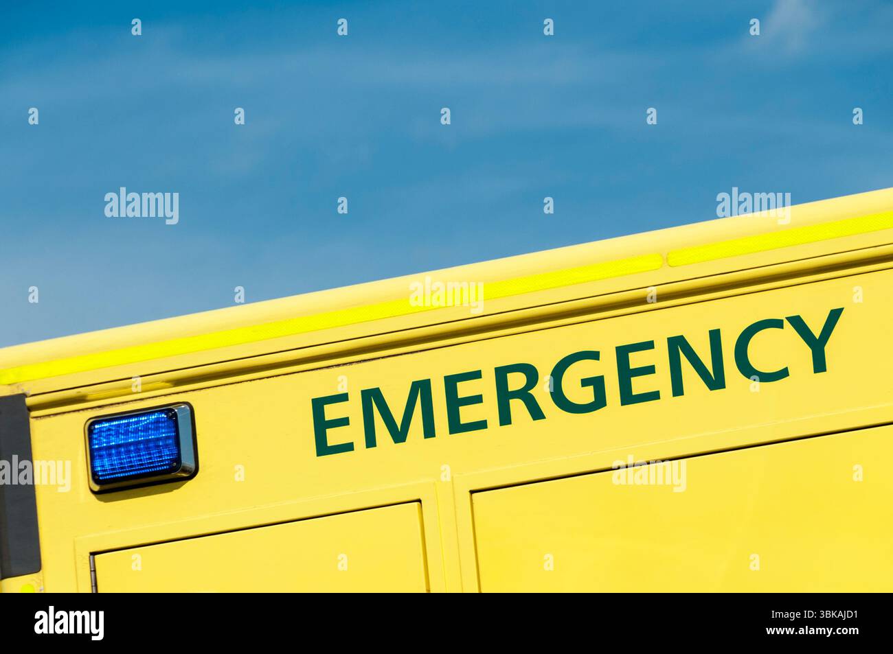 Luce blu e la parola EMERGENZA sul lato di un'ambulanza gialla di emergenza, contro un cielo blu. Foto Stock