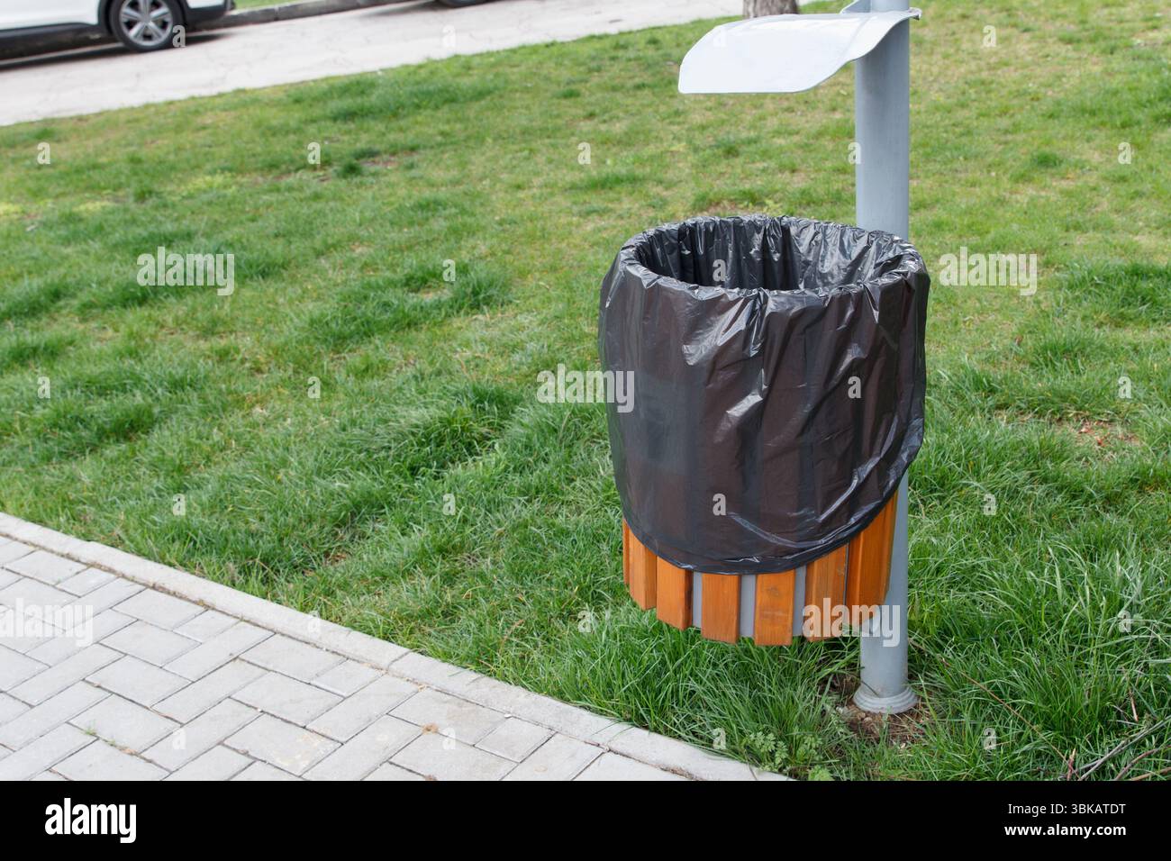 Cestino pubblico con fodera in plastica nera, spranghe in legno, sullo sfondo del parco, vicino a un marciapiede pavimentato. Concetto di pulizia urbana Foto Stock