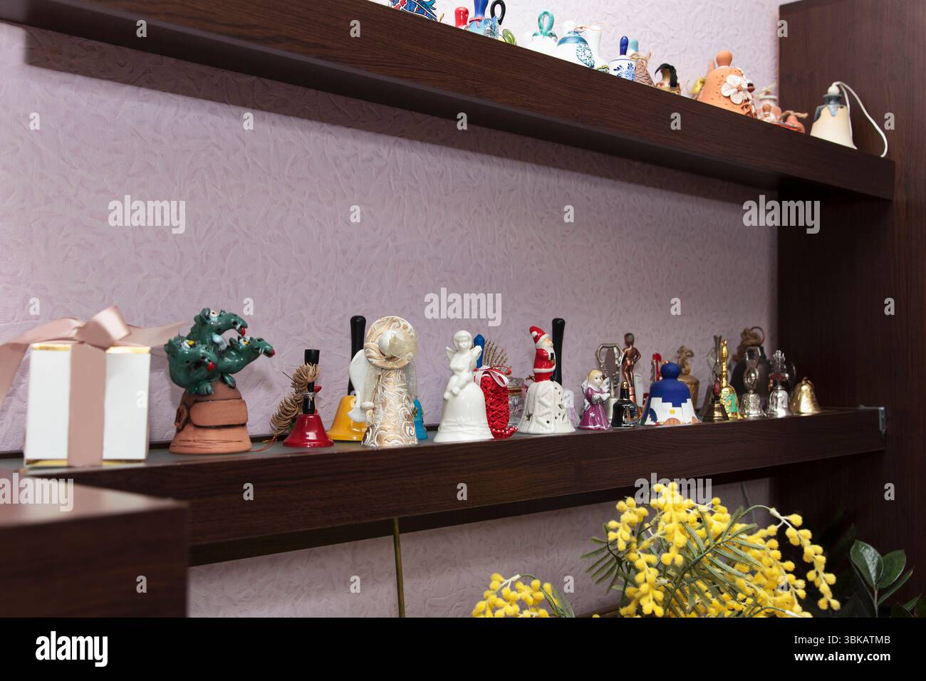 Collezione di campane decorative souvenir in ceramica e metallo su scaffali in legno scuro, fotografate all'interno su pareti in lilla testurizzata Foto Stock
