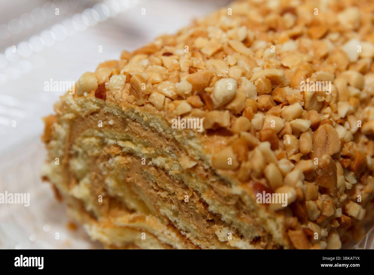 Rotolo a strati ricoperto di noci con ripieno cremoso, stile realistico, posto su uno sfondo bianco morbido, concetto di dessert Foto Stock