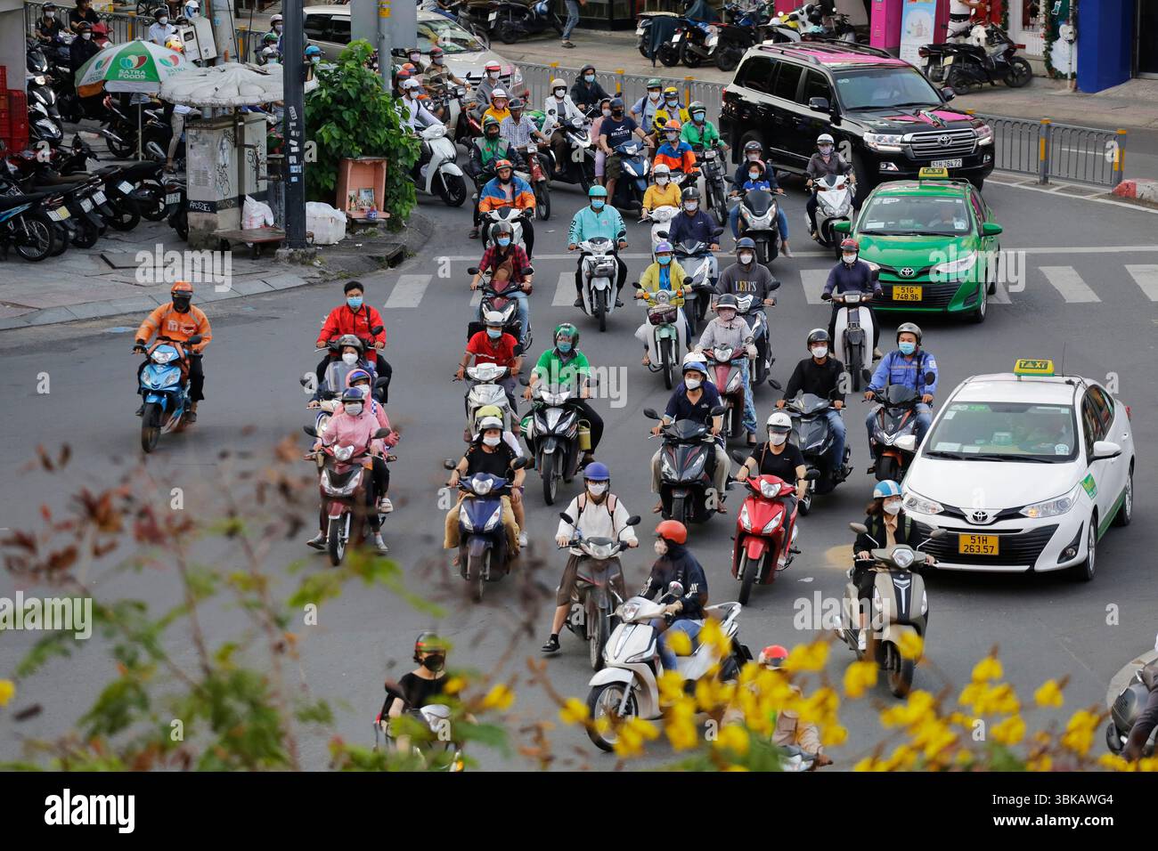 Ho chi Minh City, Vietnam - 8 dicembre 2022: Motociclisti, alcuni dei quali indossano maschere facciali, attraversano un viale a Saigon. Foto Stock