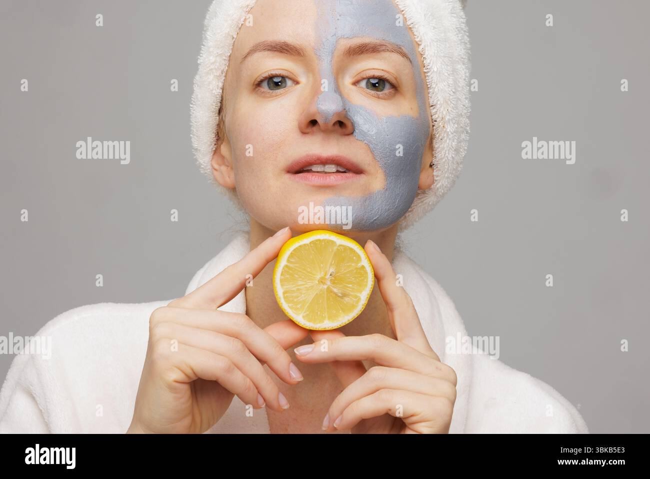 Donna con maschera cosmetica in argilla e fetta di limone, che gode di protezione contro l'invecchiamento, rassodamento e pulizia della pelle a casa. Foto Stock