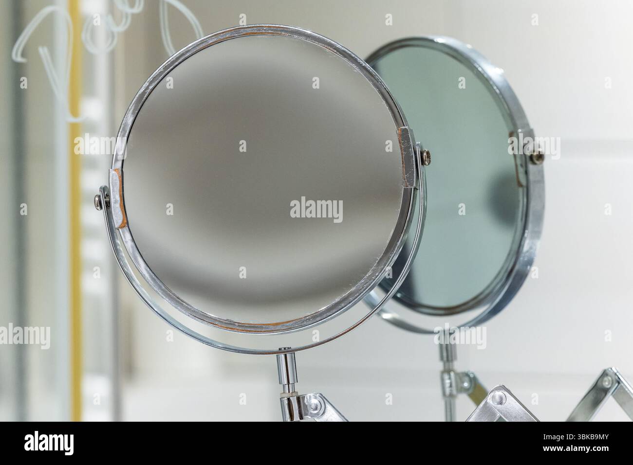 Bagno rotondo con specchio ingrandente montato a parete con pantografo. Finitura cromata del telaio dello specchietto Foto Stock