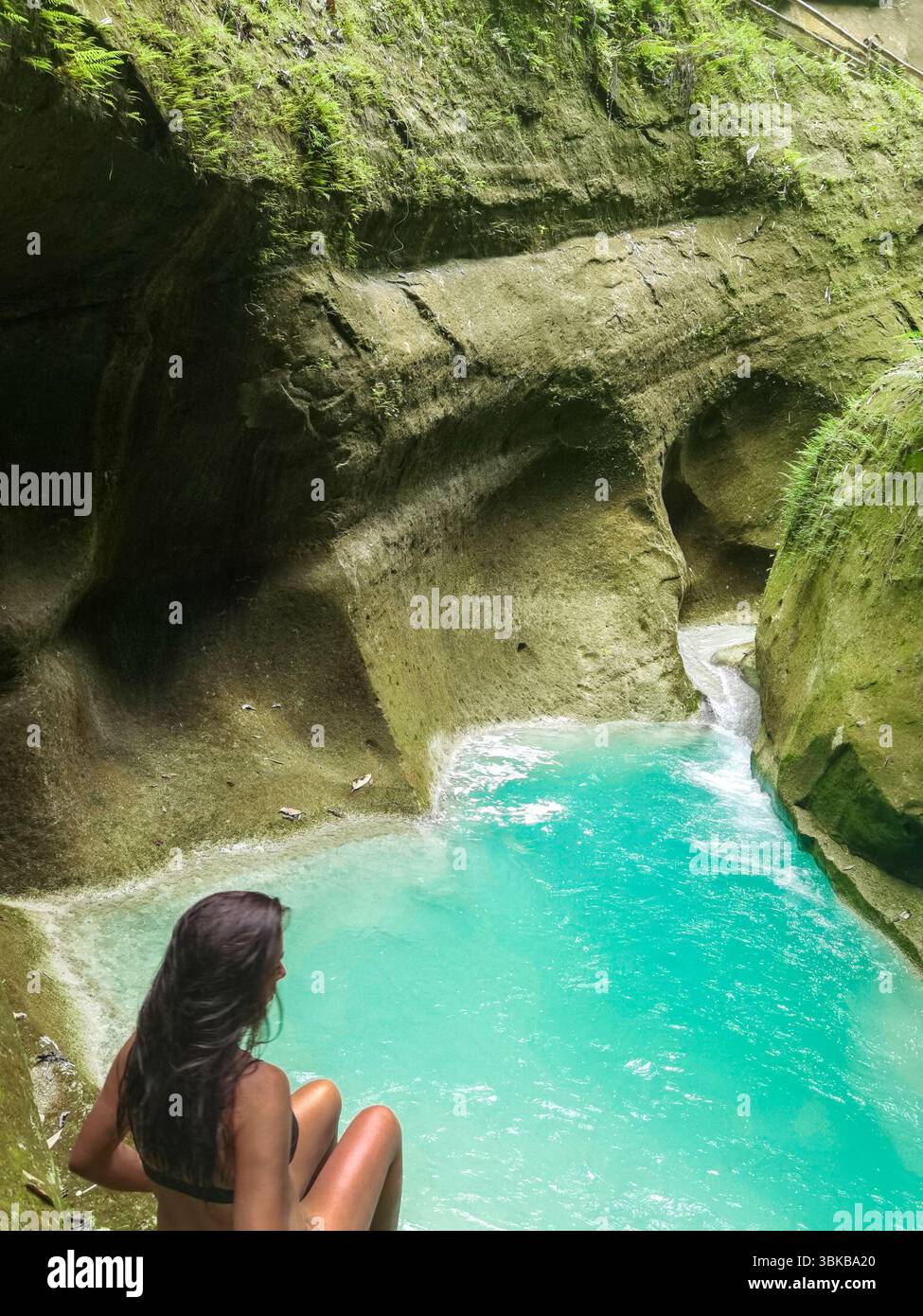 Donna seduto su una cascata nella giungla, una piscina turchese. Circondato da una lussureggiante foresta pluviale, un viaggiatore esplora il percorso accanto alle cascate Dao nelle Filippine, un ex Foto Stock
