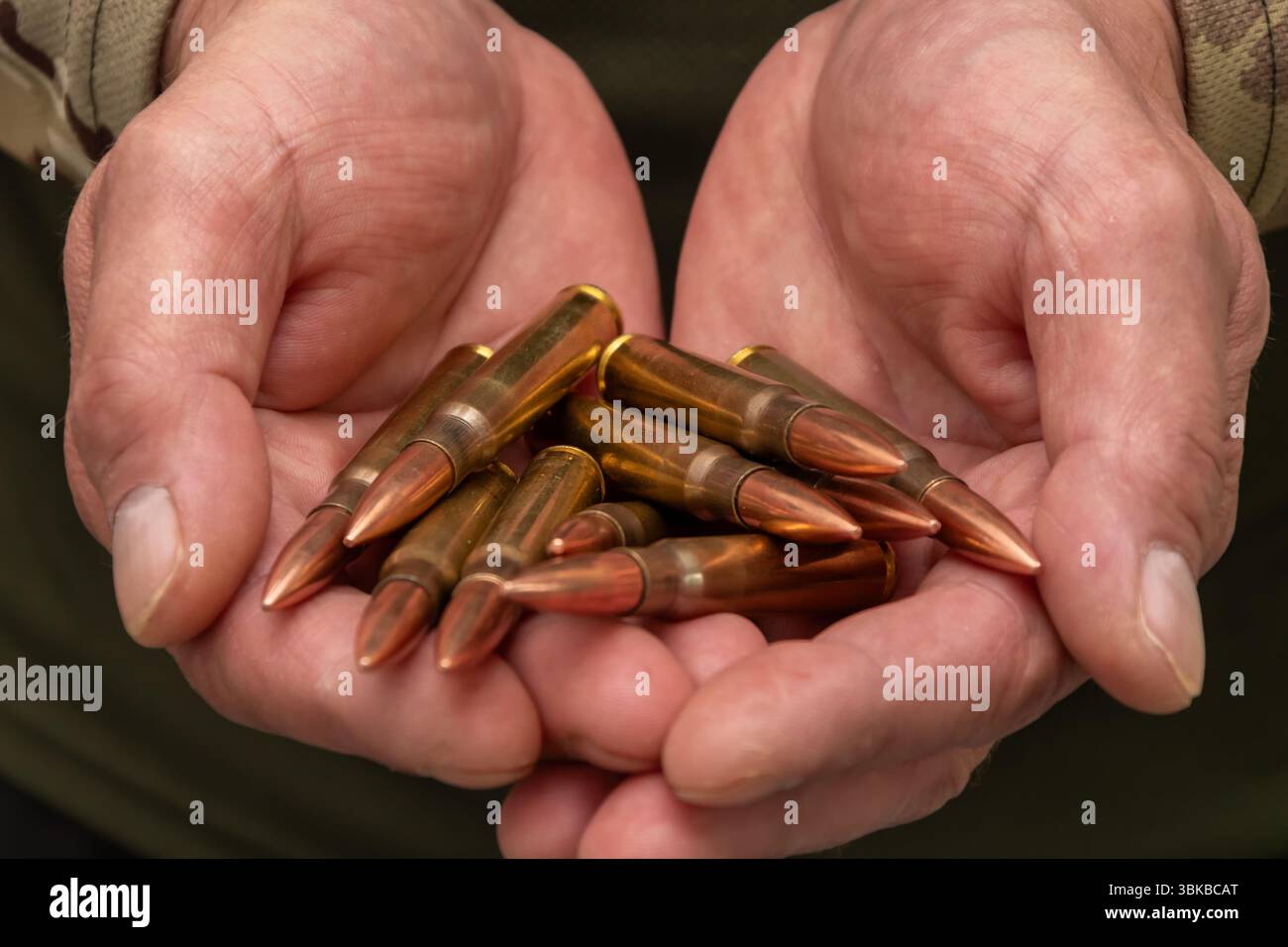 Le mani maschili in abiti militari contengono diverse cartucce di grandi dimensioni. Il primo piano simboleggia il tema della guerra, delle armi, della minaccia e dell'autodifesa Foto Stock