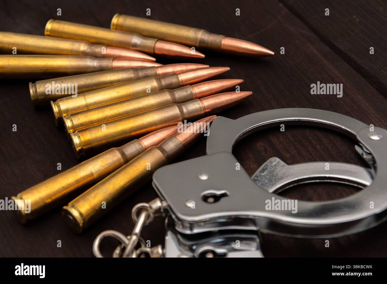 Polsini di metallo e una fila di cartucce di fucili appoggiate su una superficie di legno scuro. L'immagine simboleggia i temi del crimine, della giustizia, del pericolo e della punizione Foto Stock