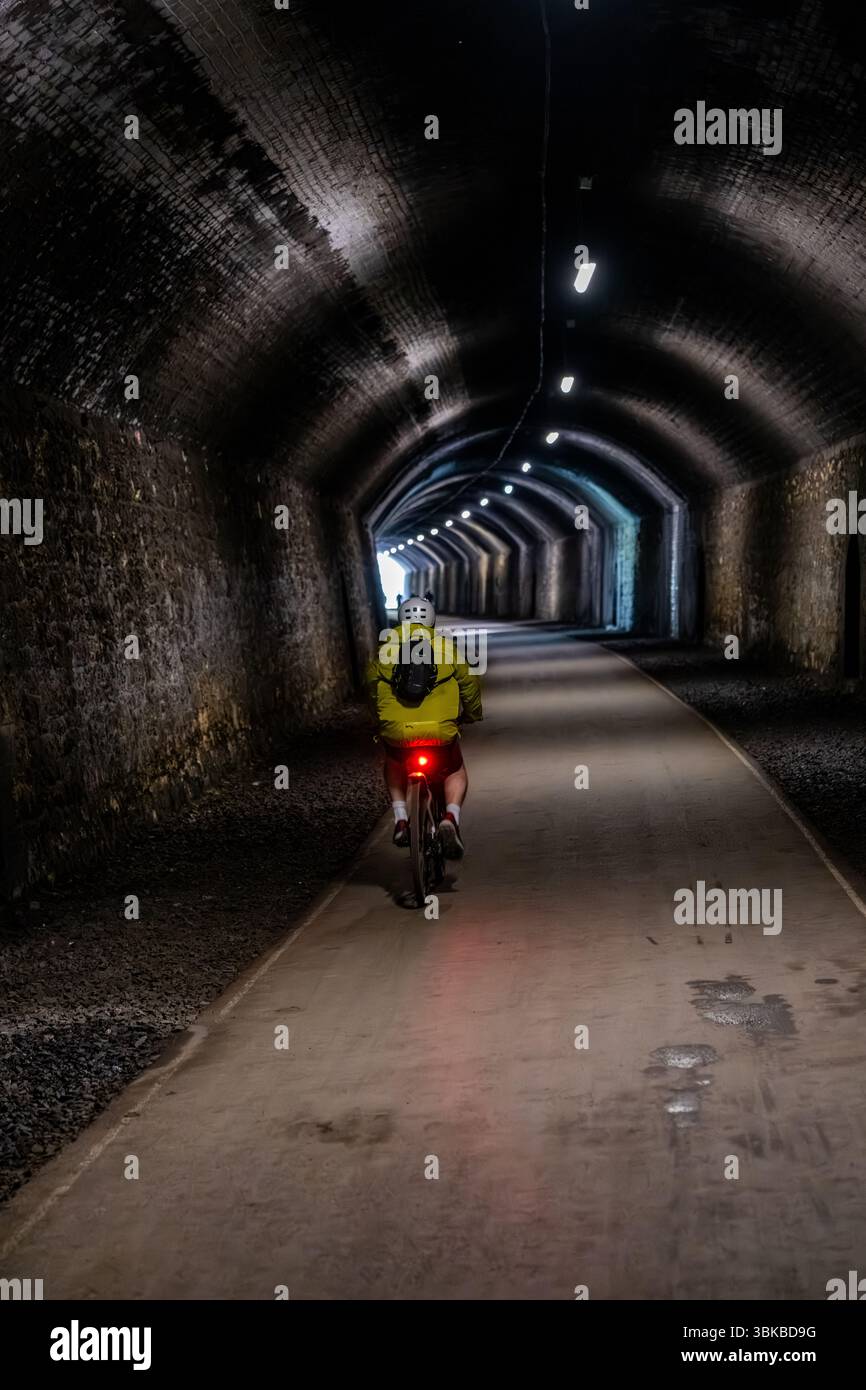 Ciclista con zaino e casco che naviga attraverso un tunnel buio, illuminato da una luce di sicurezza posteriore, per abbracciare il viaggio in avanti Foto Stock