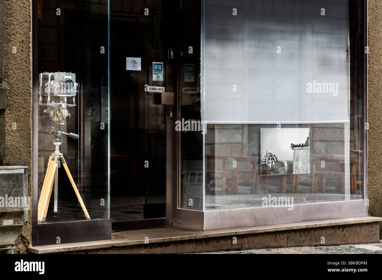 La vetrina di uno studio fotografico su Rue Haute-Vienne a Limoges, Haute-Vienne, Nouvelle-Aquitaine, Francia, mostra una vecchia macchina fotografica con corpo in metallo su un treppiede con gambe in legno. Nella vetrina di destra, una fotografia in bianco e nero di un edificio a cupola e di un angolo di casa è appesa davanti a una tenda abbassata. La porta tra di loro è vetrata. Foto Stock