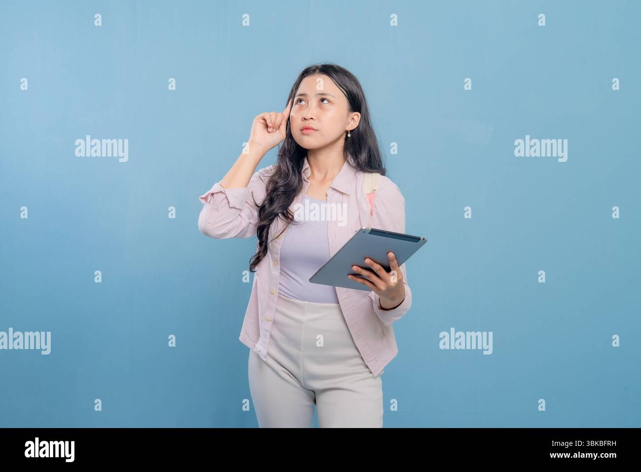 Una donna tiene in mano un tablet e guarda il soffitto. Lei è profondamente pensata Foto Stock