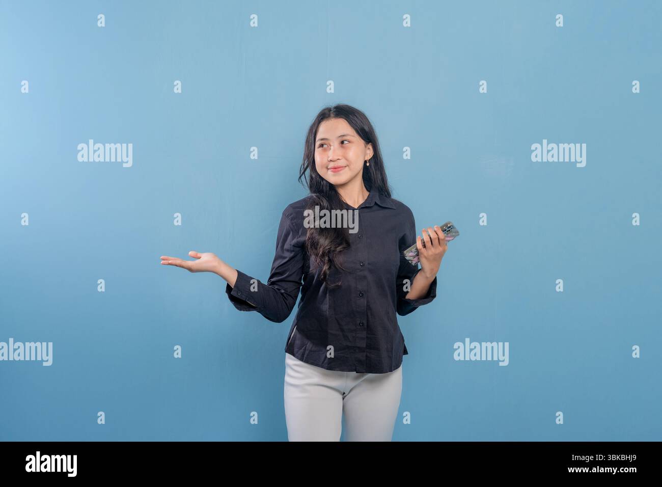 Una donna tiene un cellulare e indica qualcosa di importante. Sta sorridendo, ed è felice. Concetto di tecnologia e comunicazione moderna Foto Stock
