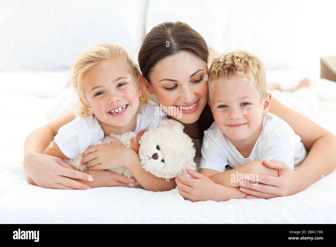Allegro i bambini con la loro madre giacente su un letto Foto Stock