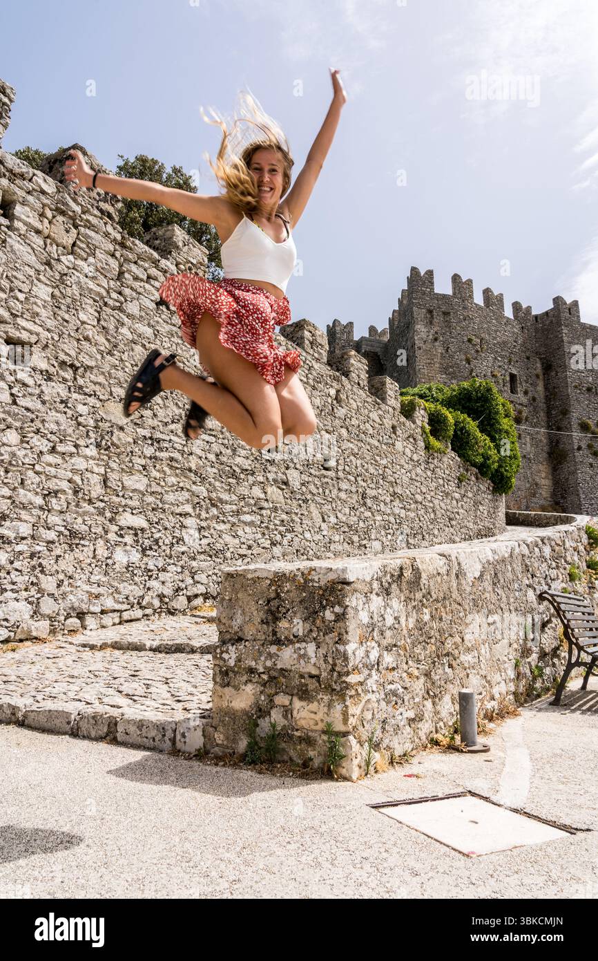 Felice turista che salta con le braccia sollevate vicino allo storico castello di Erice, in Sicilia Foto Stock
