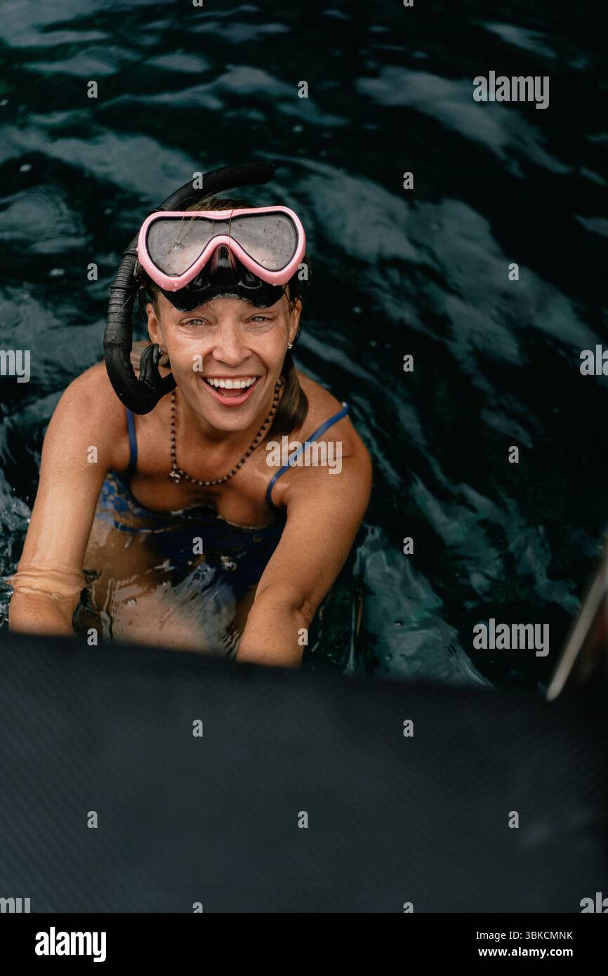 Donna sorridente con l'attrezzatura da snorkeling che sale su una barca nell'oceano tropicale Foto Stock