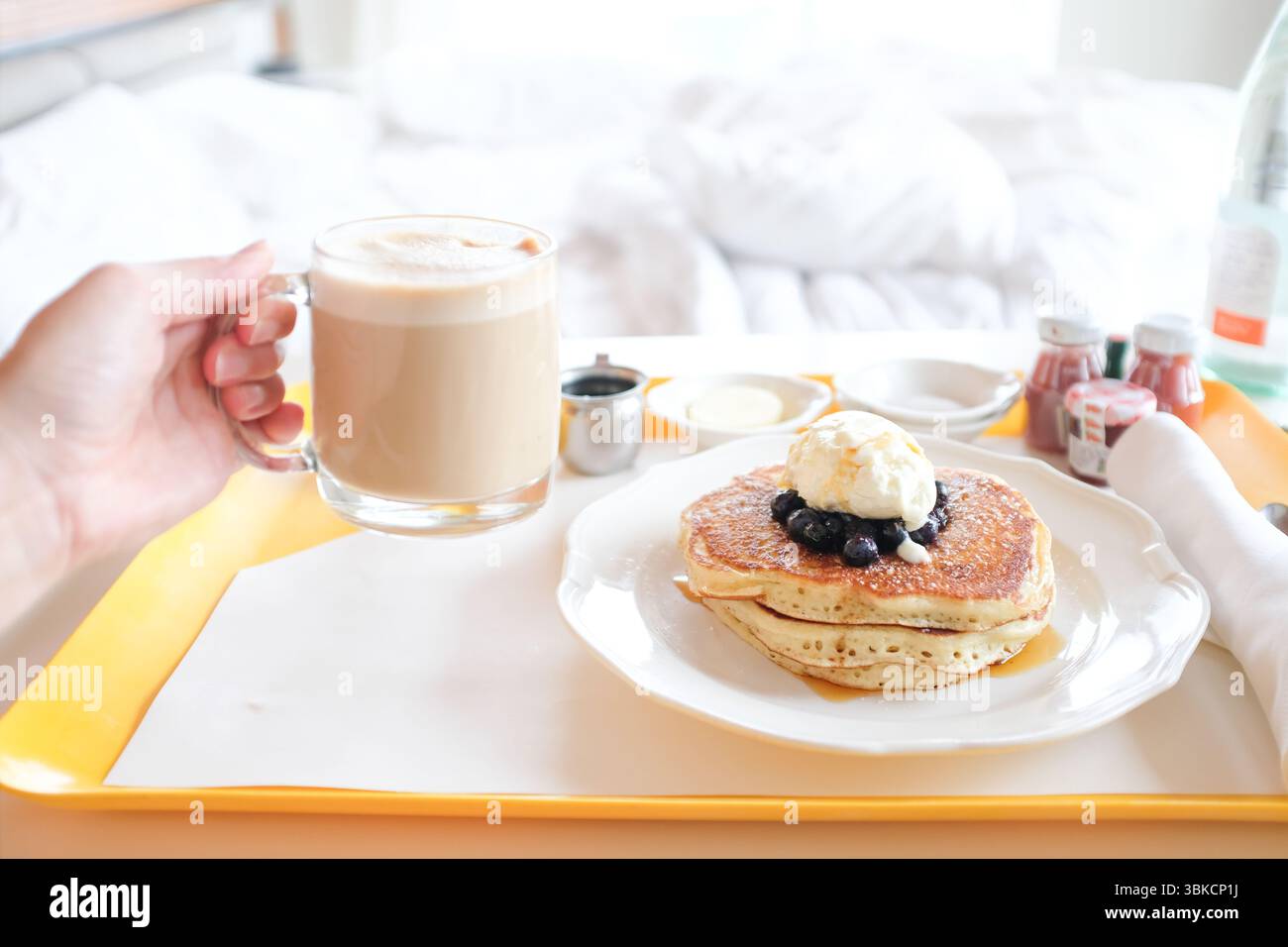 Servizio in camera con pancake e cappuccino con letto sullo sfondo Foto Stock
