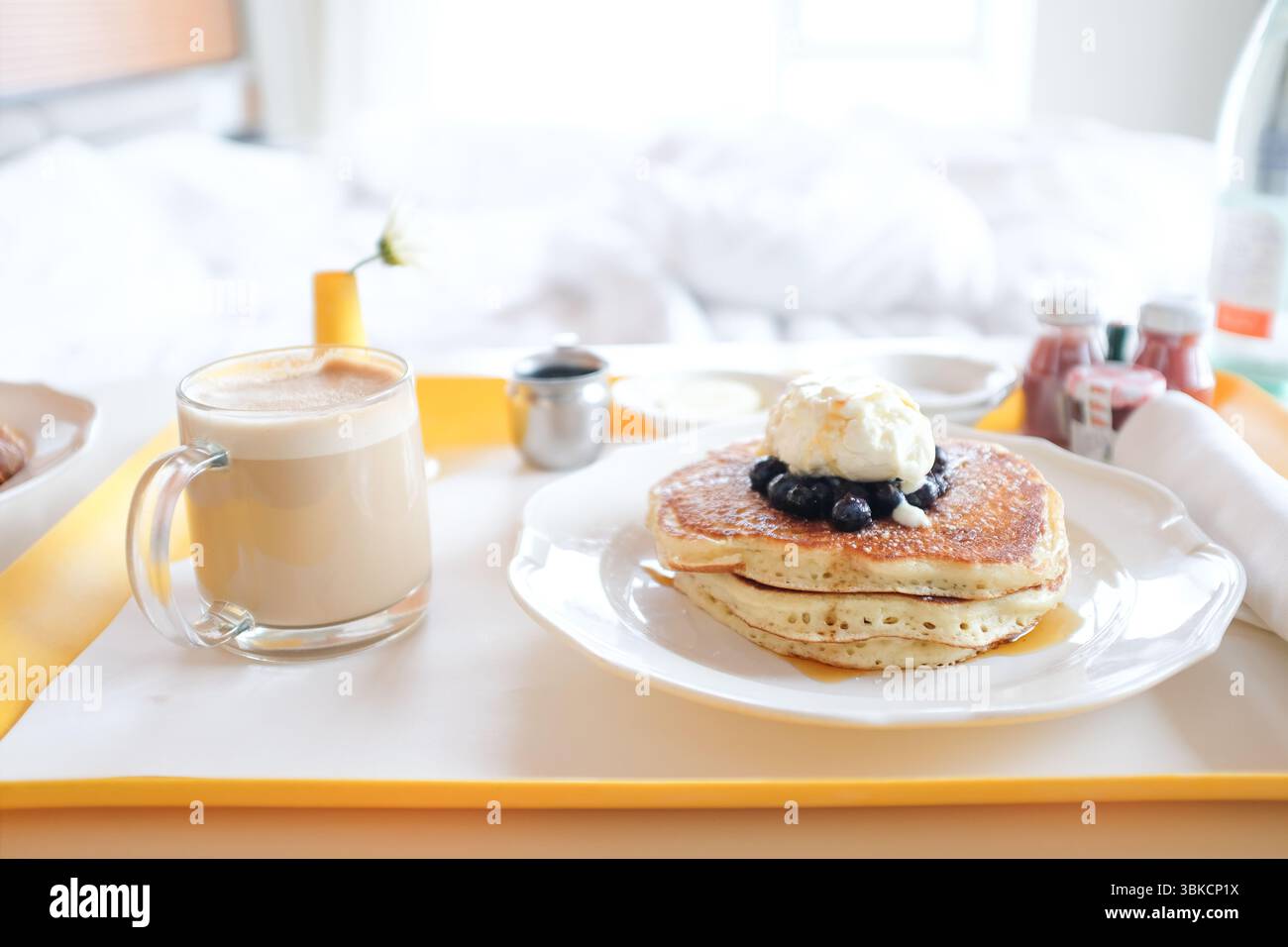 Servizio in camera con pancake e cappuccino con letto sullo sfondo Foto Stock