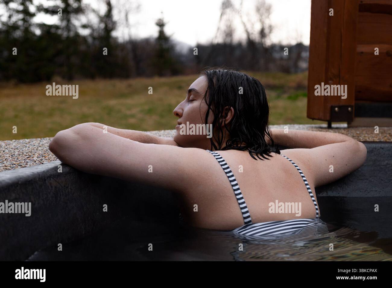 giovane donna che si gode la solitudine in una vasca idromassaggio all'aperto. Foto Stock
