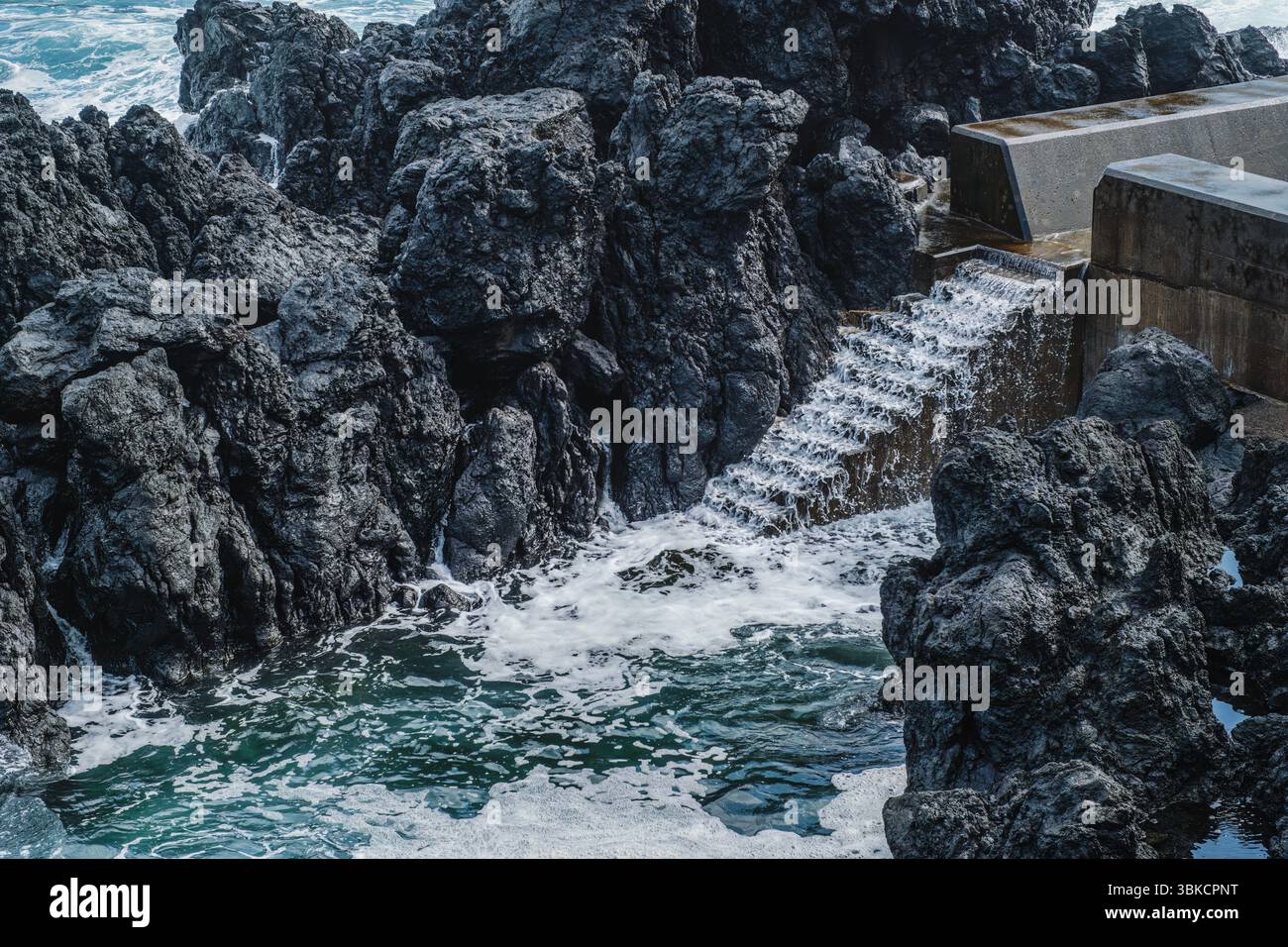 Aspra costa vulcanica con Ocean Water che si schianta sulle scale artificiali del mare a Sao Jorge, Azzorre. Piscine naturali, Dark Rocks, Foaming Waves, Atlantic Foto Stock