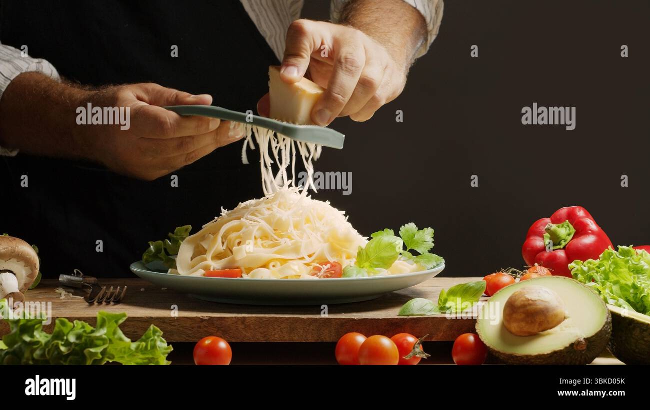 Lo chef grattugia formaggio duro su un piatto di pasta appena preparato, la Pasta è cucina mediterranea italiana tradizionale. Foto Stock
