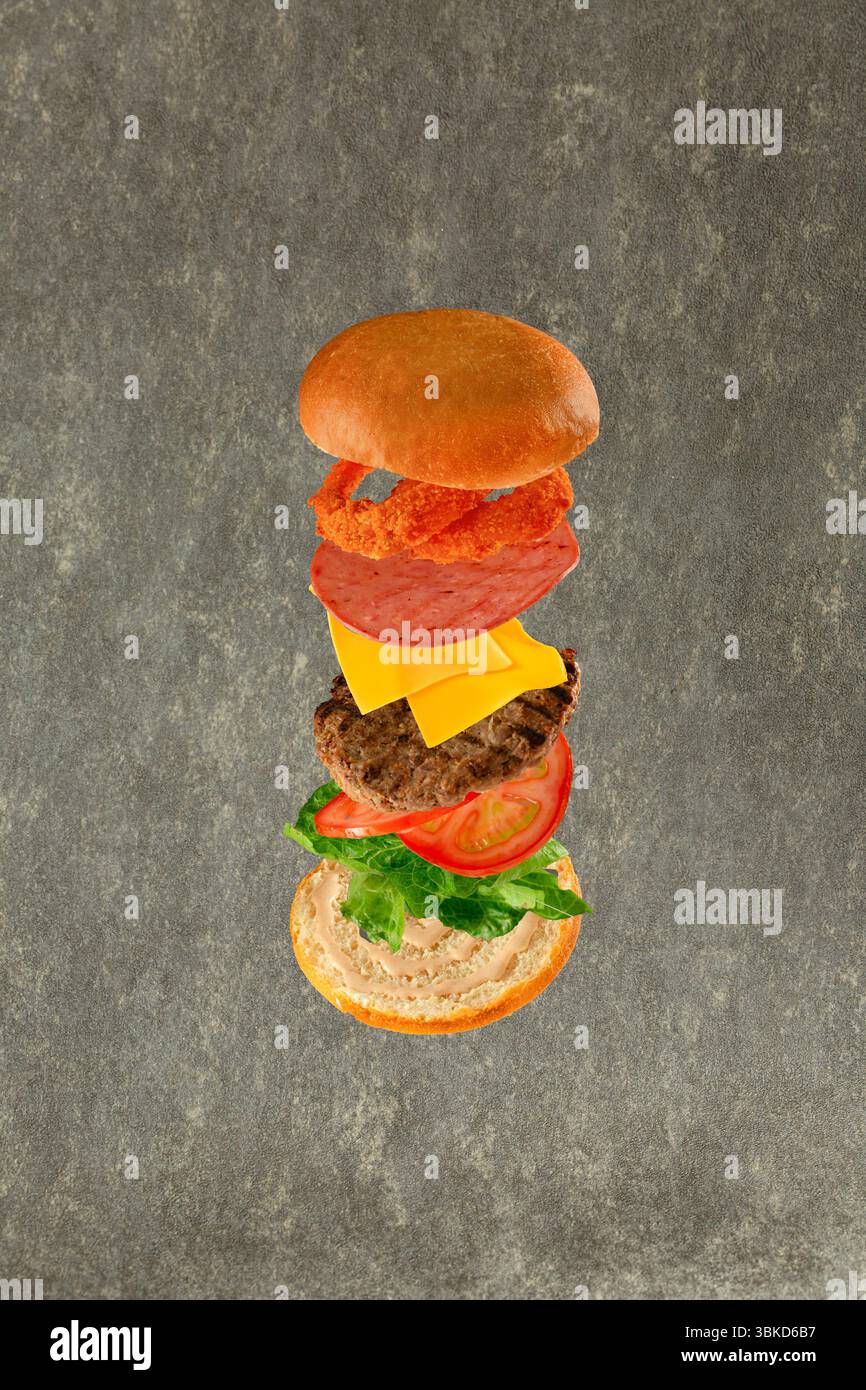 Hamburger volante con i suoi ingredienti pane lattuga pomodori formaggio di manzo salame e cipolle croccanti. Foto Stock