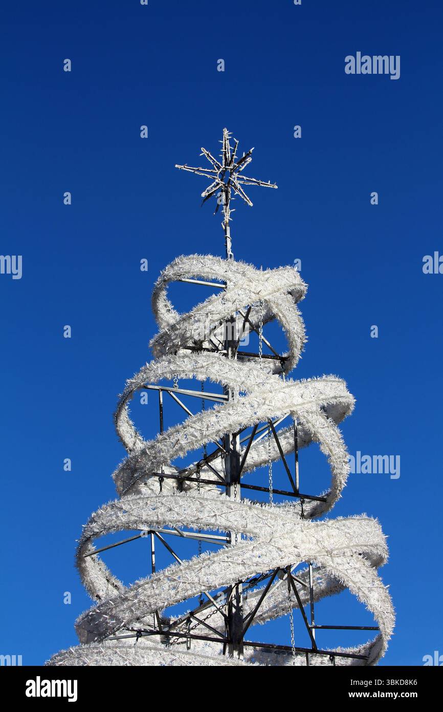 La moderna scultura all'aperto dell'albero di Natale, realizzata in una cornice metallica e una spirale bianca garland, sormontata da una stella geometrica, si distingue vividamente contro un Foto Stock
