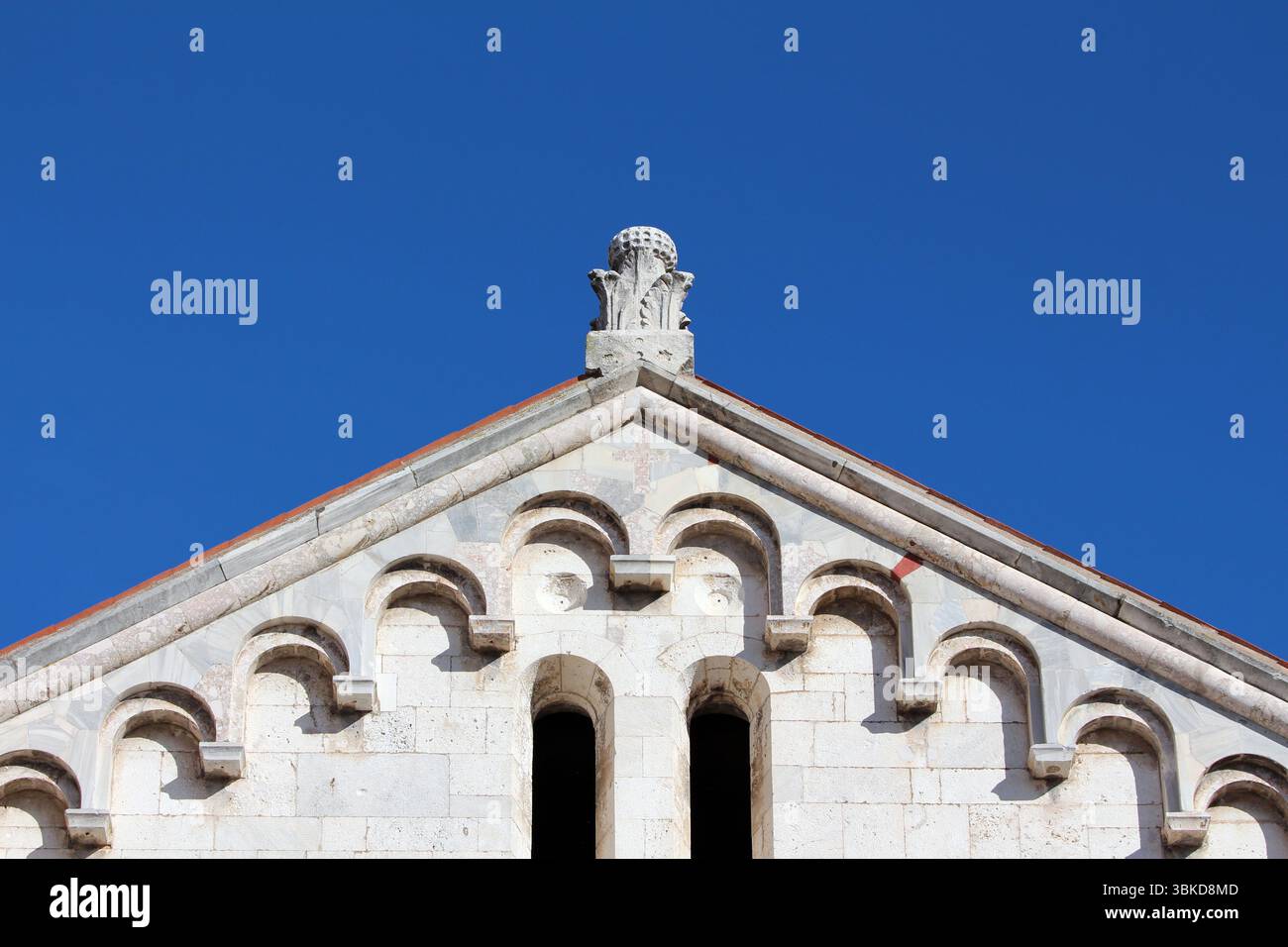 Il timpano triangolare di un edificio romanico presenta ripetuti archi in pietra e una finitura intagliata, adagiata su un cielo blu vivace e che mette in risalto la storia Foto Stock