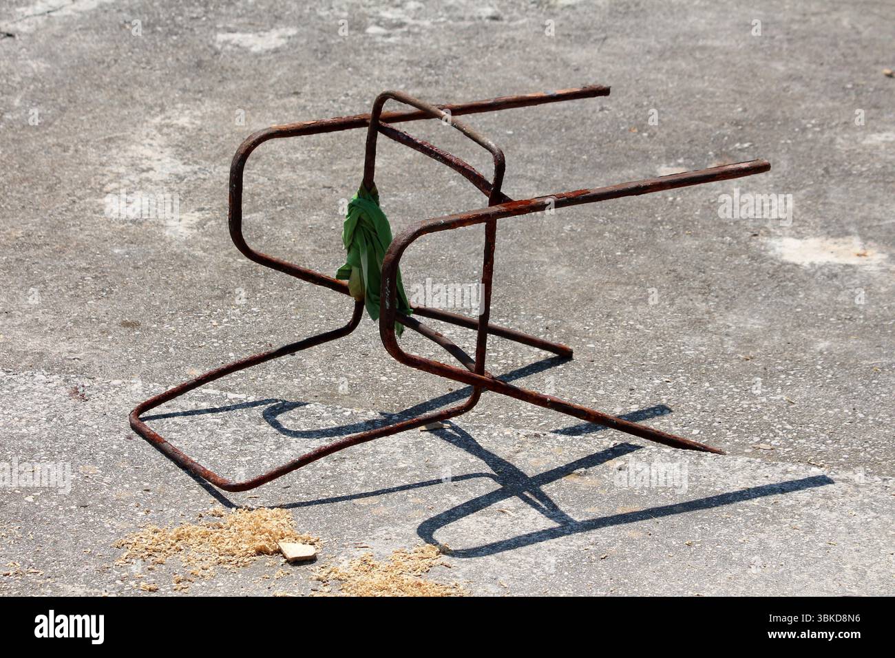 Il vecchio telaio della sedia in metallo arrugginito si capovolge su cemento grezzo, rivestito con un panno verde e circondato da segatura, evocando abbandono e degrado Foto Stock