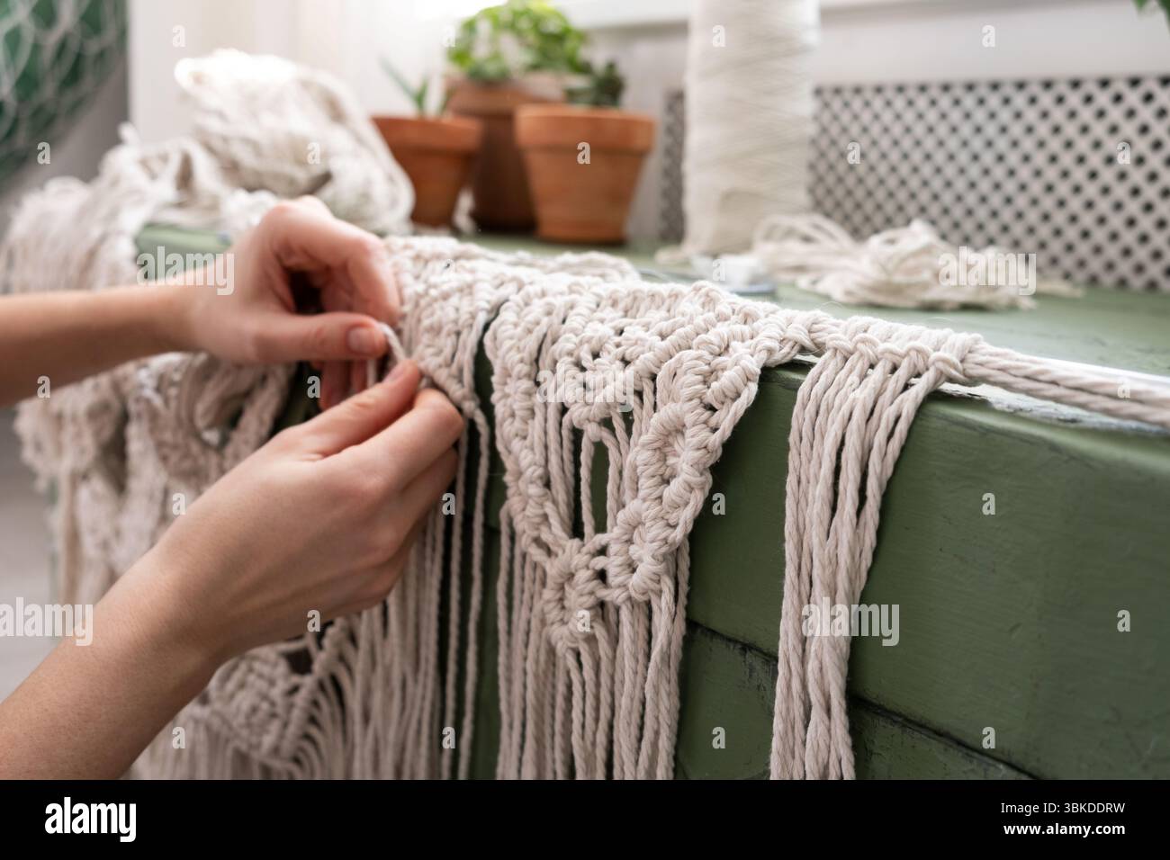 le mani delle donne tessono pannelli in macrame. fili di cotone, filati per la fabbricazione di prodotti fatti a mano per interni. Foto Stock