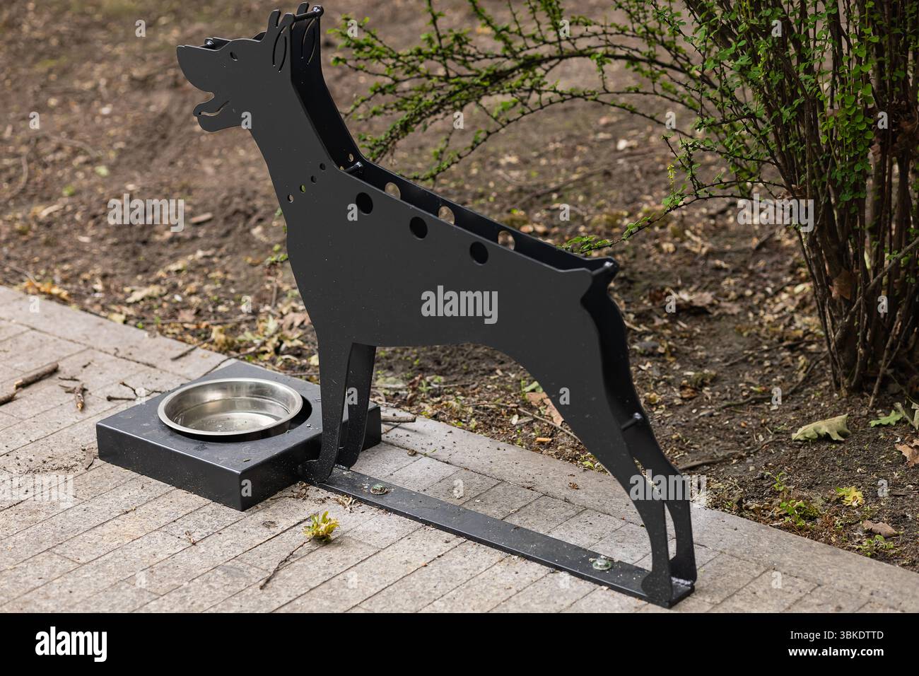 Stazione per bere a forma di cane in metallo con ciotola dell'acqua pulita installata sul marciapiede della città per l'idratazione degli animali domestici. Iniziativa per il benessere degli animali e la cura degli animali domestici di strada Foto Stock