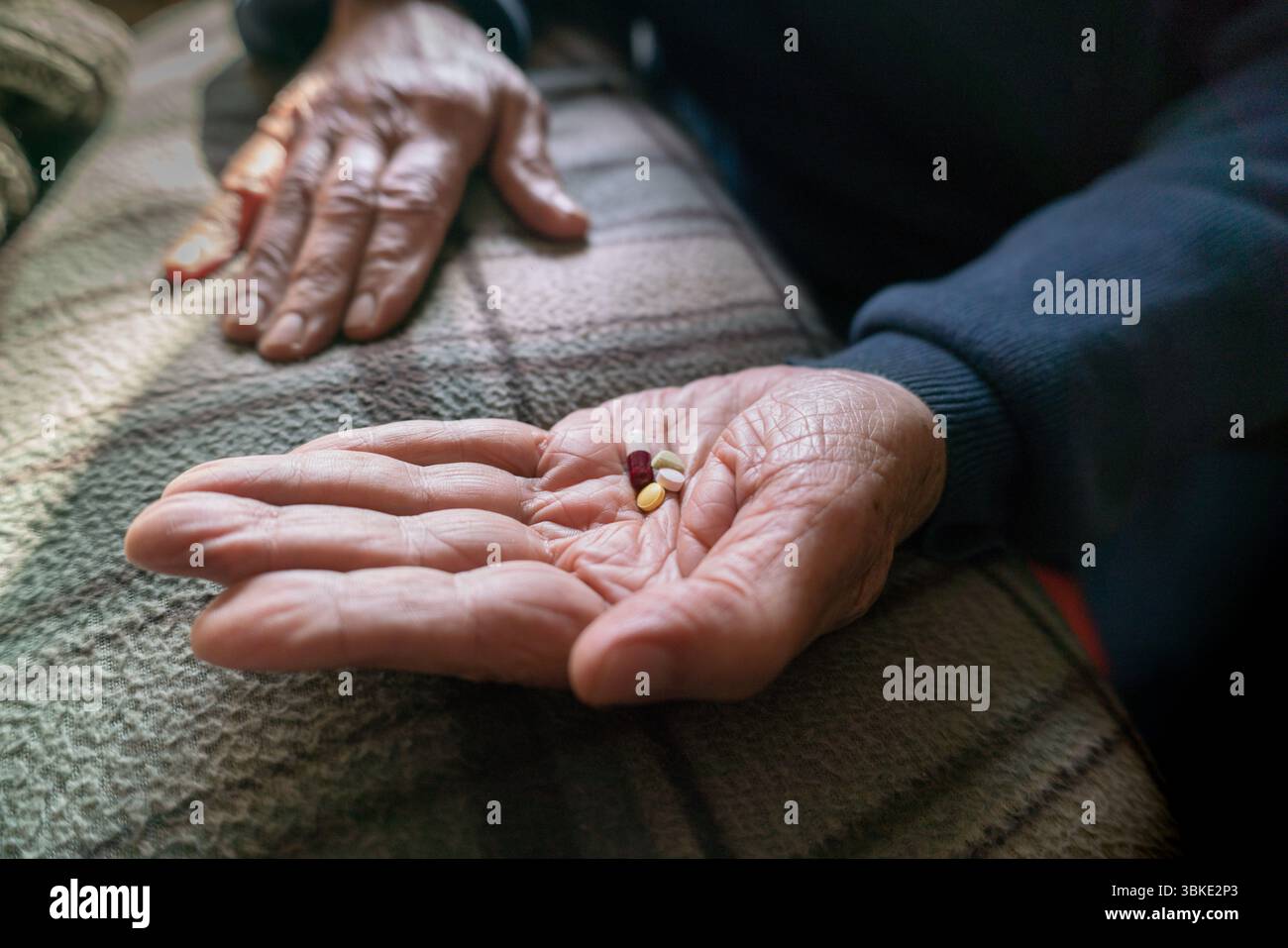 Mani anziane che tengono pillole di farmaci assortiti, simboleggiano l'assistenza sanitaria, l'invecchiamento e i farmaci quotidiani. Foto Stock