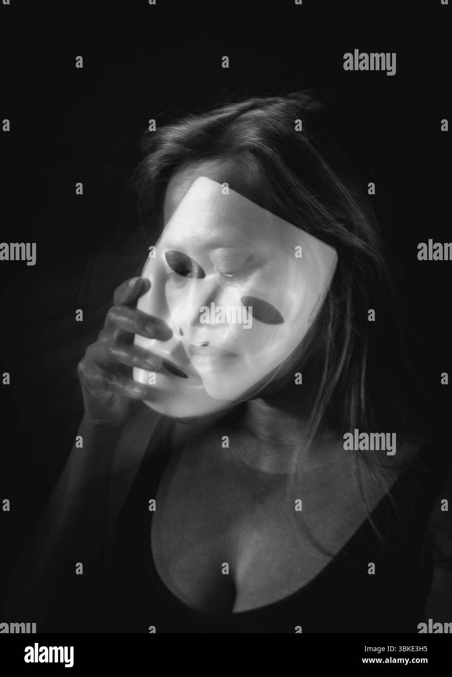 Ritratto a lunga esposizione in bianco e nero di una donna che tiene una maschera traslucida con sfocatura del movimento Foto Stock