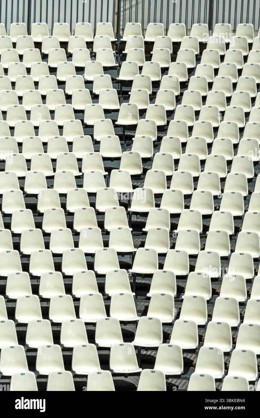 File di posti bianchi vuoti riempiono un grande stadio, creando uno schema uniforme. Foto Stock