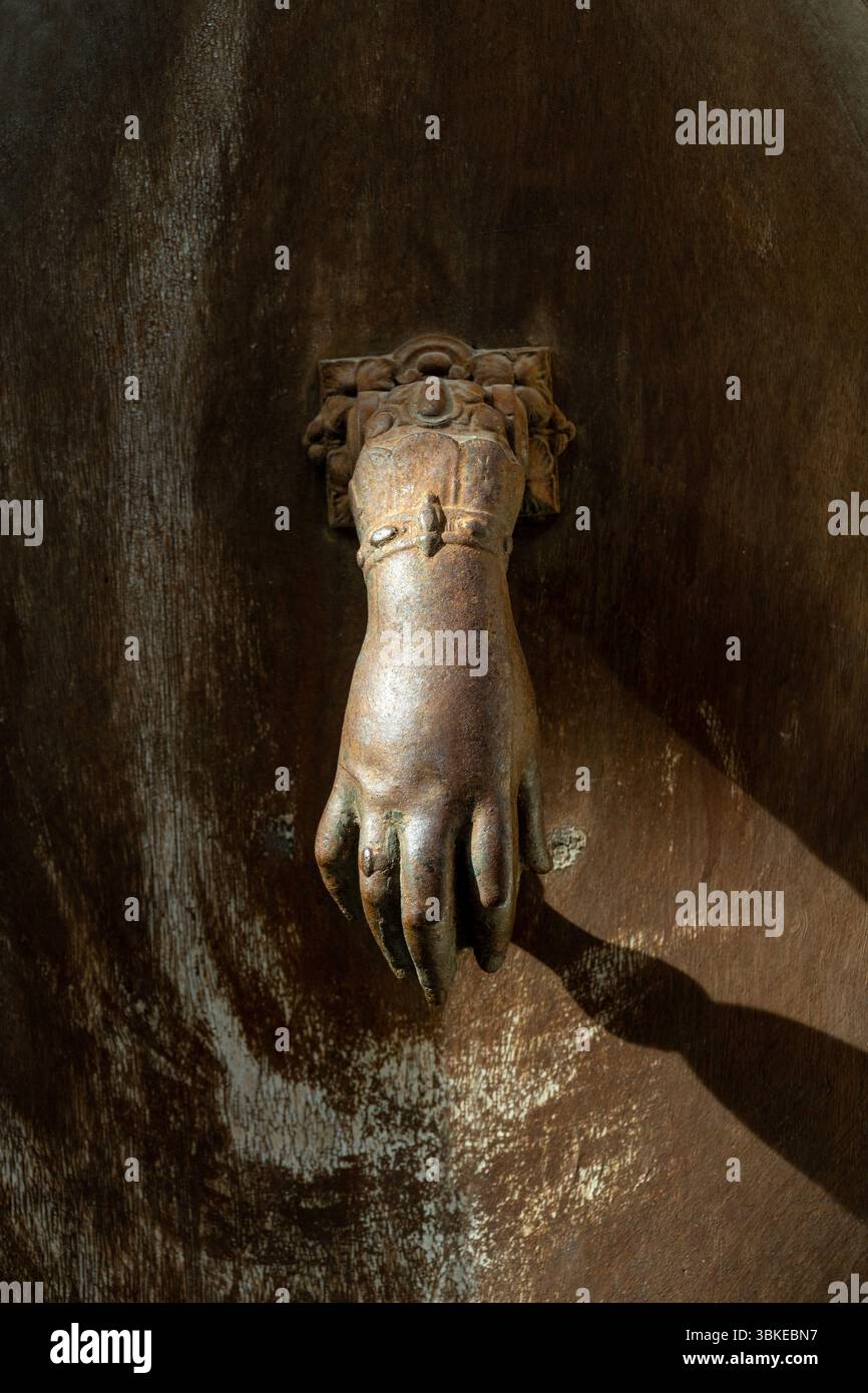 Un battitoio decorativo a forma di mano è saldamente montato su una porta in legno resistente agli agenti atmosferici che mostra ricche texture e un fascino antico dell'Auvergne. Francia Foto Stock