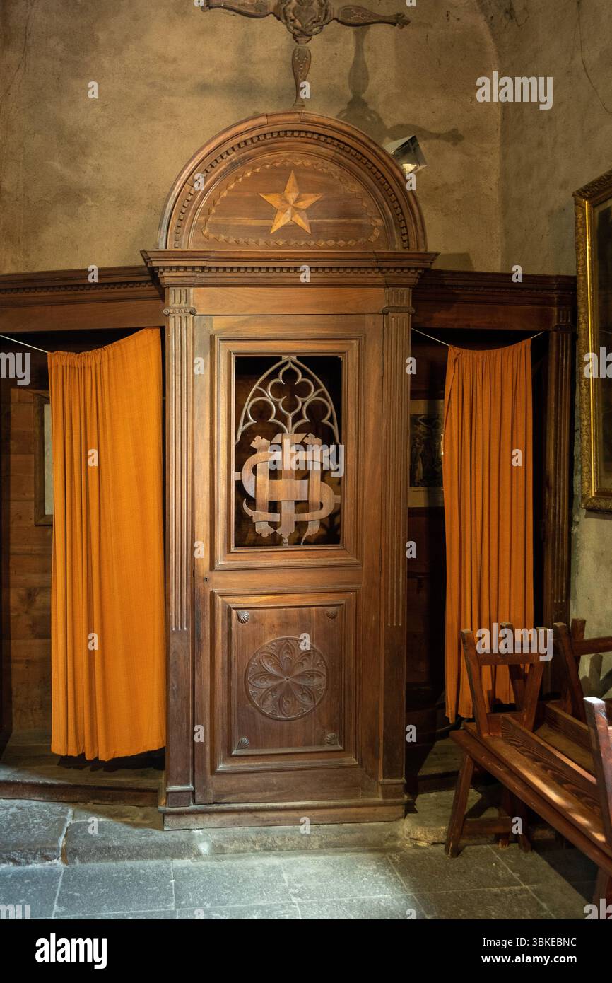 Uno stand confessionale in legno splendidamente realizzato sorge in una chiesa storica, caratterizzata da dettagli ornati e vivaci tende arancioni. Auvergne. Francia Foto Stock