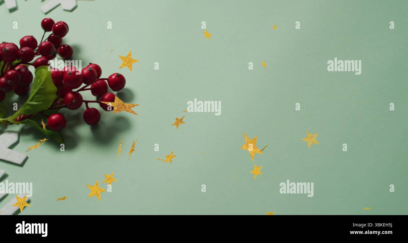 Disposizione di rametti di frutti rossi con foglie verdi su un tavolo verde, con glitter a stella dorata, spazio di copia Foto Stock