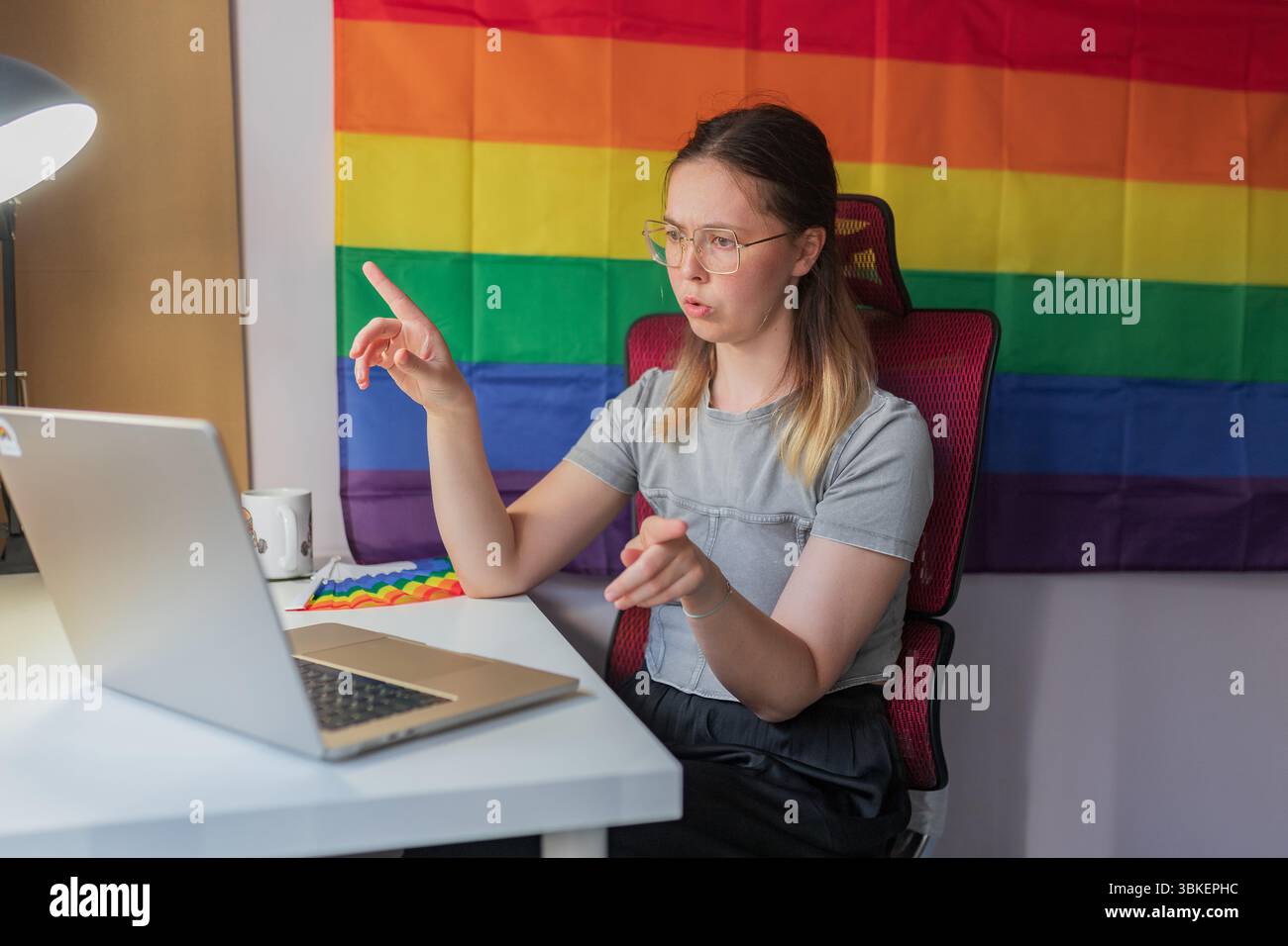 Gesti femminili con il dito sollevato durante le intense comunicazioni online a casa. Una giovane donna seria fa un gesto appuntito mentre guarda il notebook e piove Foto Stock