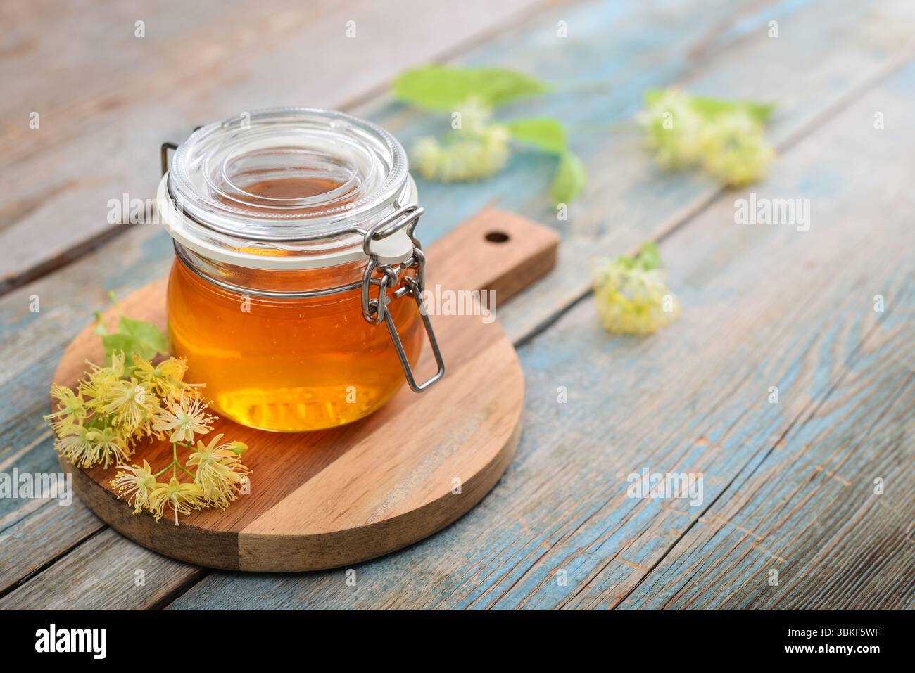 Miele di tiglio in vaso di vetro con dipper di miele di legno e fiori di tiglio su fondo di legno Foto Stock