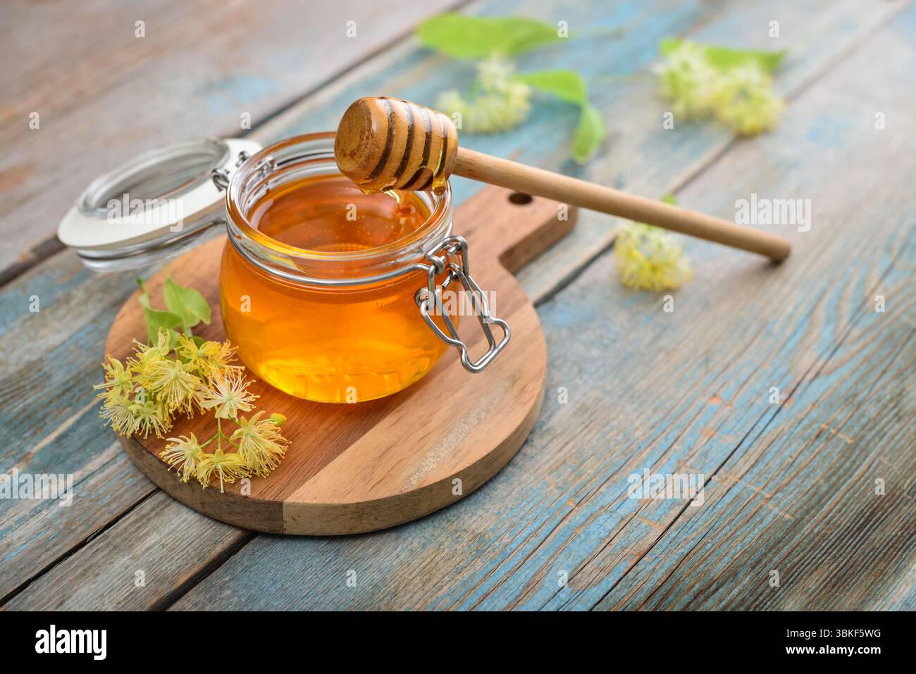 Miele di tiglio in vaso di vetro con dipper di miele di legno e fiori di tiglio su fondo di legno Foto Stock